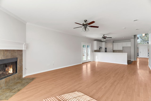 unfurnished living room featuring light hardwood / wood-style floors, a tiled fireplace, ornamental molding, and plenty of natural light