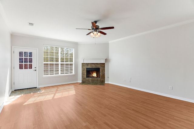 unfurnished living room featuring ornamental molding, ceiling fan, hardwood / wood-style floors, and a tiled fireplace