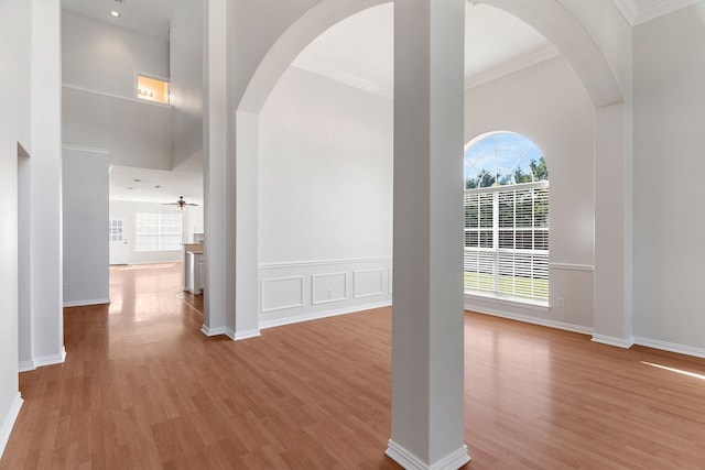 interior space featuring a towering ceiling, light wood-type flooring, crown molding, and a healthy amount of sunlight