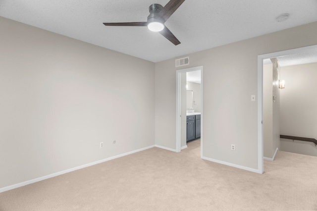 unfurnished bedroom featuring ensuite bath, ceiling fan, light carpet, and a textured ceiling