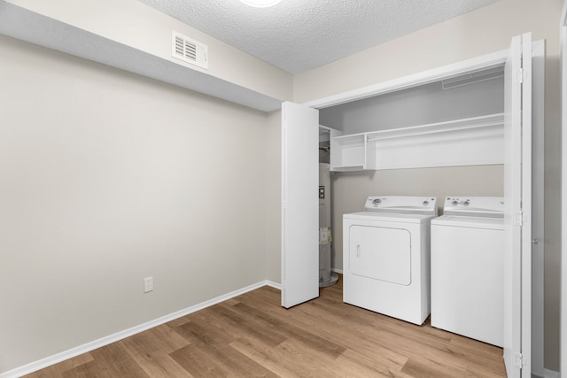 washroom with light wood-type flooring, separate washer and dryer, a textured ceiling, and water heater