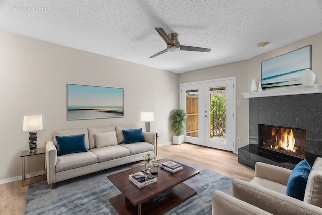 living room with ceiling fan, french doors, wood-type flooring, a textured ceiling, and a tiled fireplace