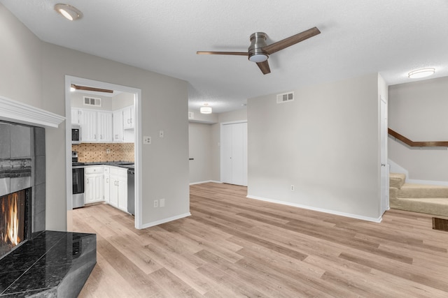 living room featuring a fireplace, a textured ceiling, light hardwood / wood-style floors, and ceiling fan