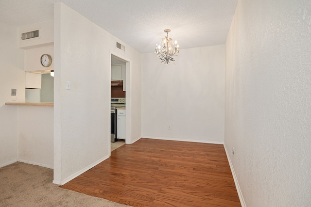 empty room with hardwood / wood-style flooring, a textured ceiling, and an inviting chandelier