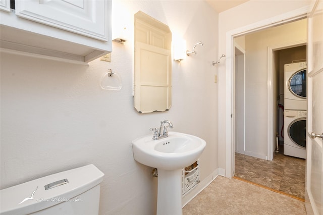 bathroom with toilet, stacked washing maching and dryer, and sink