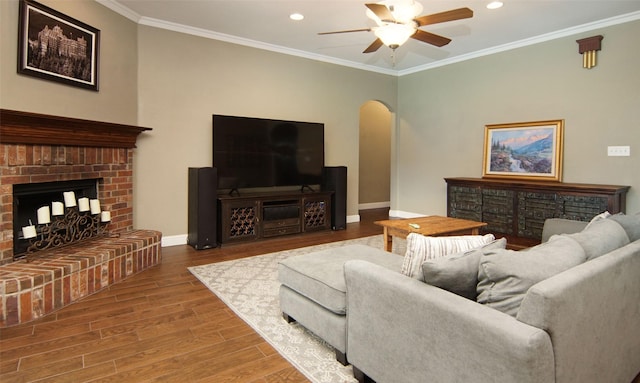 living room with hardwood / wood-style floors, a brick fireplace, ceiling fan, and crown molding