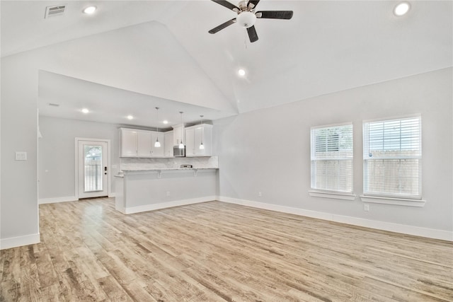 unfurnished living room with a wealth of natural light, ceiling fan, light hardwood / wood-style flooring, and high vaulted ceiling