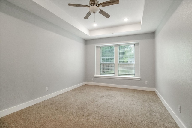 empty room featuring carpet flooring, a raised ceiling, and ceiling fan