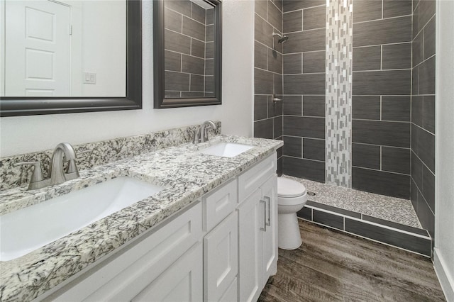 bathroom with tiled shower, wood-type flooring, vanity, and toilet