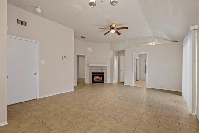 unfurnished living room with ceiling fan, vaulted ceiling, a textured ceiling, a tiled fireplace, and light tile patterned flooring