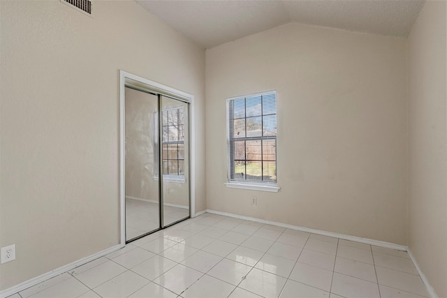 unfurnished bedroom with a closet, light tile patterned flooring, and vaulted ceiling