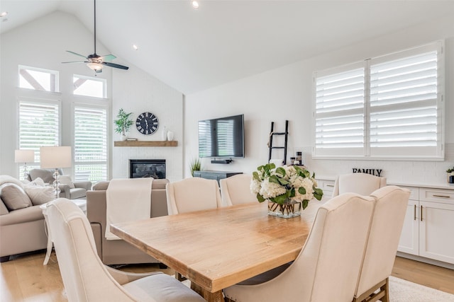 dining area with ceiling fan, light hardwood / wood-style floors, a fireplace, and vaulted ceiling