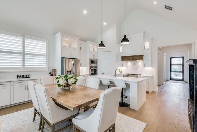 dining area with light wood-type flooring and high vaulted ceiling