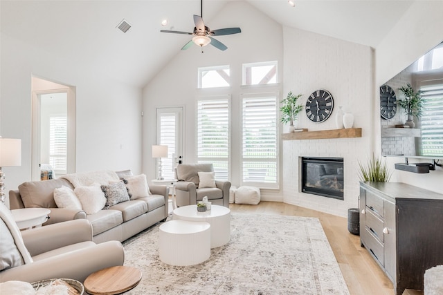 living room featuring ceiling fan, a fireplace, high vaulted ceiling, and light wood-type flooring