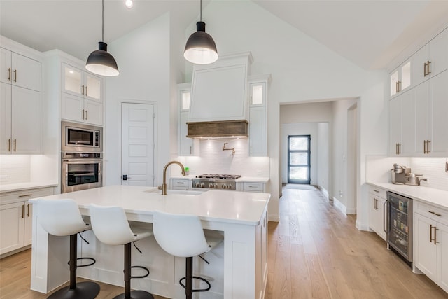 kitchen featuring white cabinetry, sink, beverage cooler, stainless steel appliances, and an island with sink