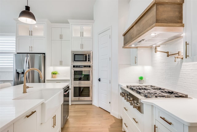 kitchen with decorative backsplash, appliances with stainless steel finishes, premium range hood, pendant lighting, and white cabinets