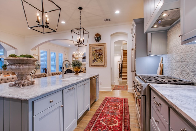 kitchen with custom exhaust hood, stainless steel appliances, a kitchen island with sink, sink, and hanging light fixtures