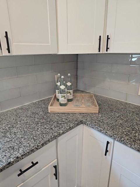 room details with decorative backsplash, white cabinetry, and dark stone countertops