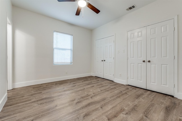 unfurnished bedroom with ceiling fan, light wood-type flooring, and two closets