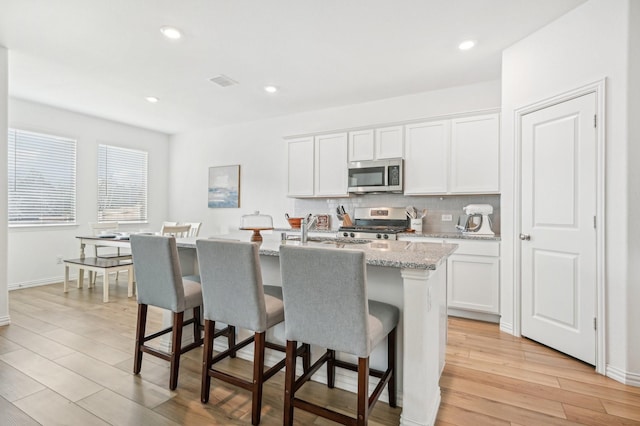 kitchen featuring visible vents, a kitchen island with sink, tasteful backsplash, light wood-style floors, and appliances with stainless steel finishes