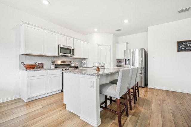 kitchen with white cabinetry, stainless steel appliances, a kitchen island with sink, and light stone counters