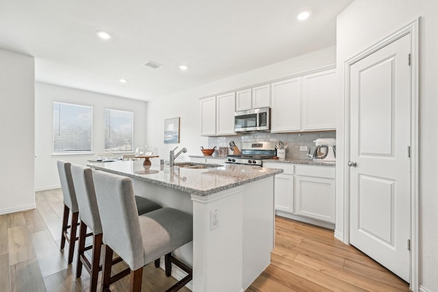 kitchen featuring visible vents, backsplash, a sink, appliances with stainless steel finishes, and a kitchen island with sink