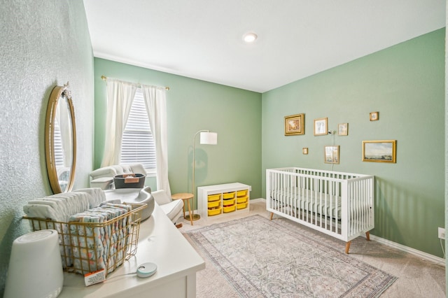 carpeted bedroom featuring a nursery area and baseboards