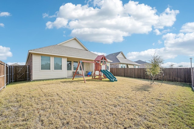 rear view of house featuring a lawn, a playground, and a fenced backyard