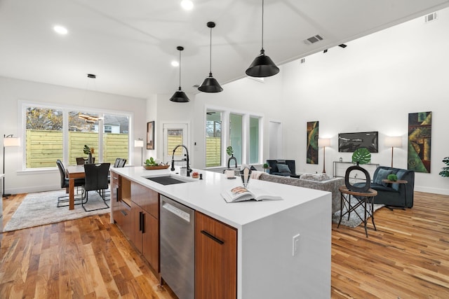 kitchen featuring sink, hanging light fixtures, light hardwood / wood-style flooring, stainless steel dishwasher, and an island with sink