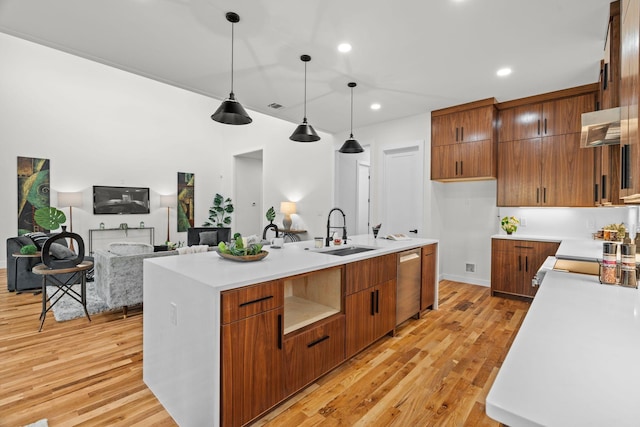 kitchen featuring stainless steel dishwasher, a kitchen island with sink, sink, light hardwood / wood-style floors, and hanging light fixtures