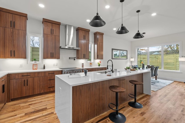 kitchen with a kitchen breakfast bar, light wood-type flooring, wall chimney exhaust hood, hanging light fixtures, and an island with sink