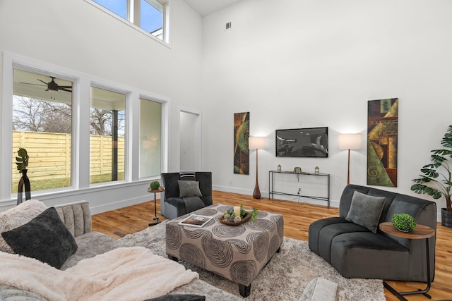 living room with ceiling fan, a high ceiling, and light wood-type flooring