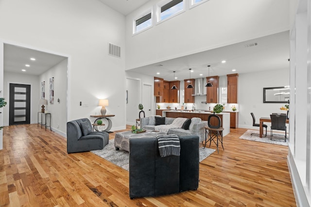 living room featuring a towering ceiling, sink, and light hardwood / wood-style flooring