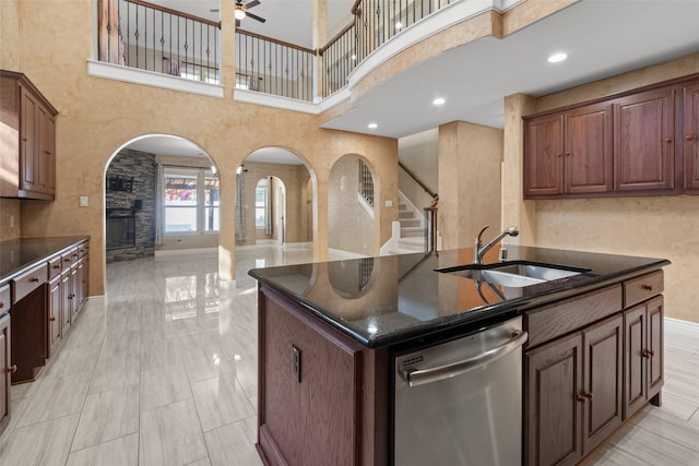 kitchen featuring stainless steel dishwasher, a kitchen island with sink, sink, a fireplace, and a high ceiling