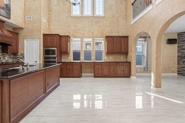 kitchen featuring sink, decorative backsplash, a towering ceiling, appliances with stainless steel finishes, and a chandelier