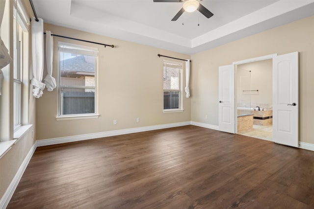 unfurnished bedroom featuring ceiling fan, dark hardwood / wood-style floors, connected bathroom, and a tray ceiling