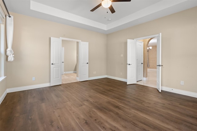 unfurnished bedroom featuring a tray ceiling, ceiling fan, and dark wood-type flooring