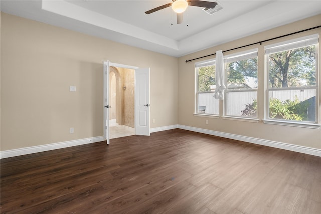 empty room with a raised ceiling, ceiling fan, and dark hardwood / wood-style floors