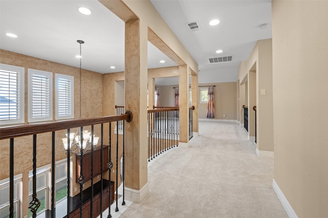 corridor with light colored carpet and a notable chandelier