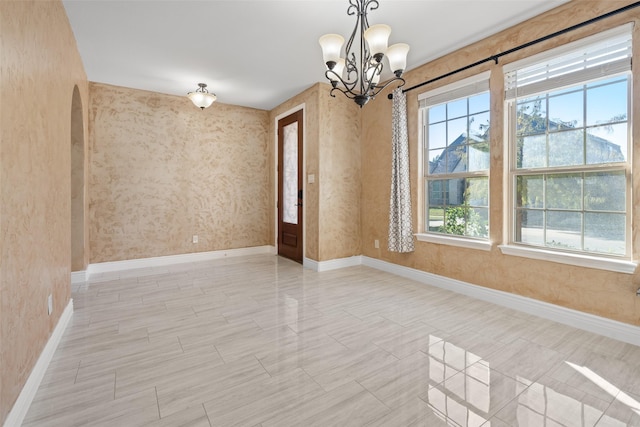 spare room featuring a healthy amount of sunlight and a chandelier