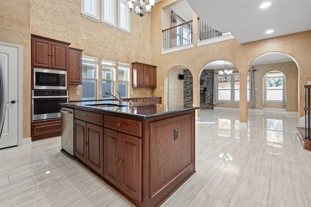 kitchen with sink, stainless steel appliances, a high ceiling, a notable chandelier, and a kitchen island with sink