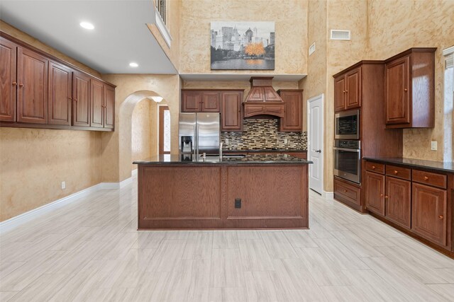 kitchen featuring appliances with stainless steel finishes, an island with sink, a high ceiling, and custom exhaust hood