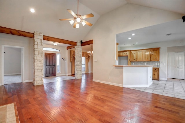 unfurnished living room featuring ceiling fan with notable chandelier, light hardwood / wood-style floors, and vaulted ceiling