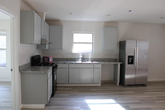 kitchen featuring black range with electric stovetop, sink, light stone counters, stainless steel refrigerator with ice dispenser, and light wood-type flooring