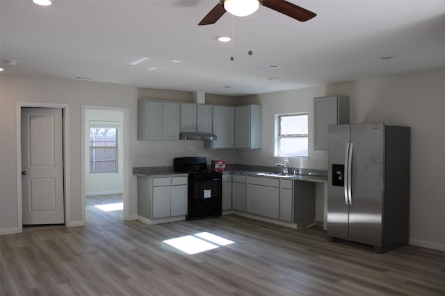 kitchen featuring black range oven, sink, stainless steel refrigerator with ice dispenser, light hardwood / wood-style flooring, and gray cabinets