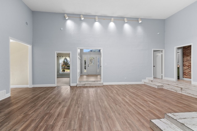 unfurnished living room with hardwood / wood-style floors, rail lighting, and a high ceiling