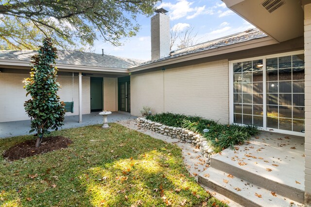 view of exterior entry featuring a yard and a patio