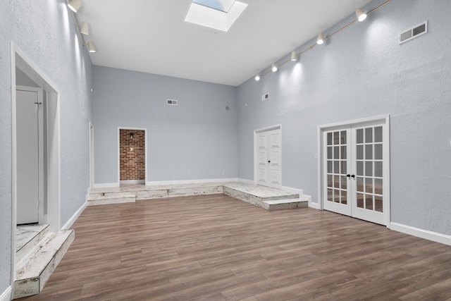 unfurnished living room with hardwood / wood-style floors, a skylight, french doors, and a high ceiling