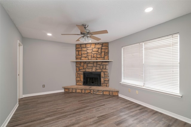 unfurnished living room with a stone fireplace, ceiling fan, and dark hardwood / wood-style floors