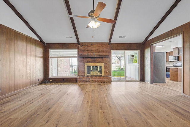 unfurnished living room featuring wood walls, a brick fireplace, vaulted ceiling with beams, ceiling fan, and light wood-type flooring